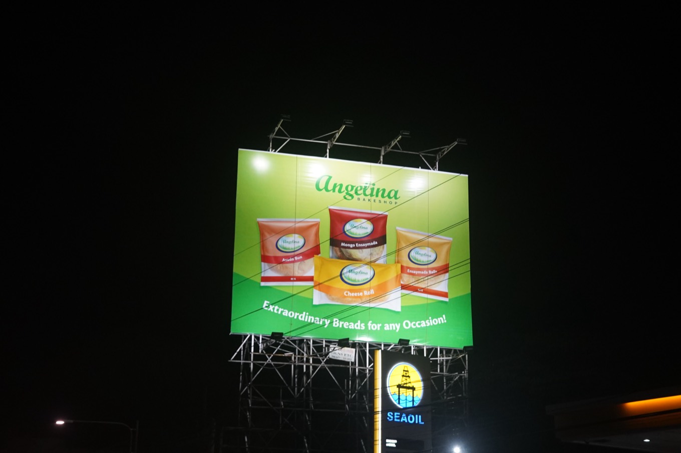 An Angelina Bakeshop billboard lit up against the night sky, showing three of their bread packs above the line &ldquo;Extraordinary Breads for any Occasion&rdquo;.